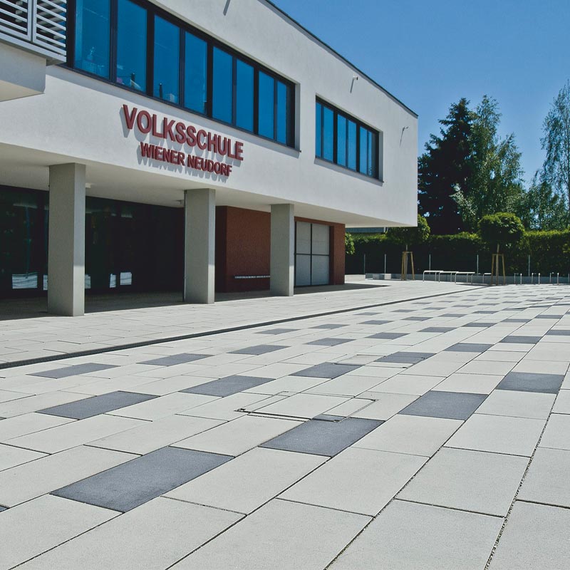 Volkschule Wiener Neudorf Magnum, sivá-antracitová betónové dlažby Friedl Steinwerke Volkschule Wiener Neudorf Magnum, sivá-antracitová betónové dlažby Friedl Steinwerke