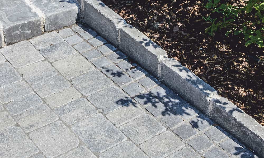 Piazza Grado, bridlica tieňovaná; Grado kocka, antracitová, Grado tvárnica, antracitová (schod) a Grado univerzálna dlažobná platňa, antracitová (obruby) Piazza Grado, bridlica tieňovaná; Grado kocka, antracitová, Grado tvárnica, antracitová (schod) a Grado univerzálna dlažobná platňa, antracitová (obruby)